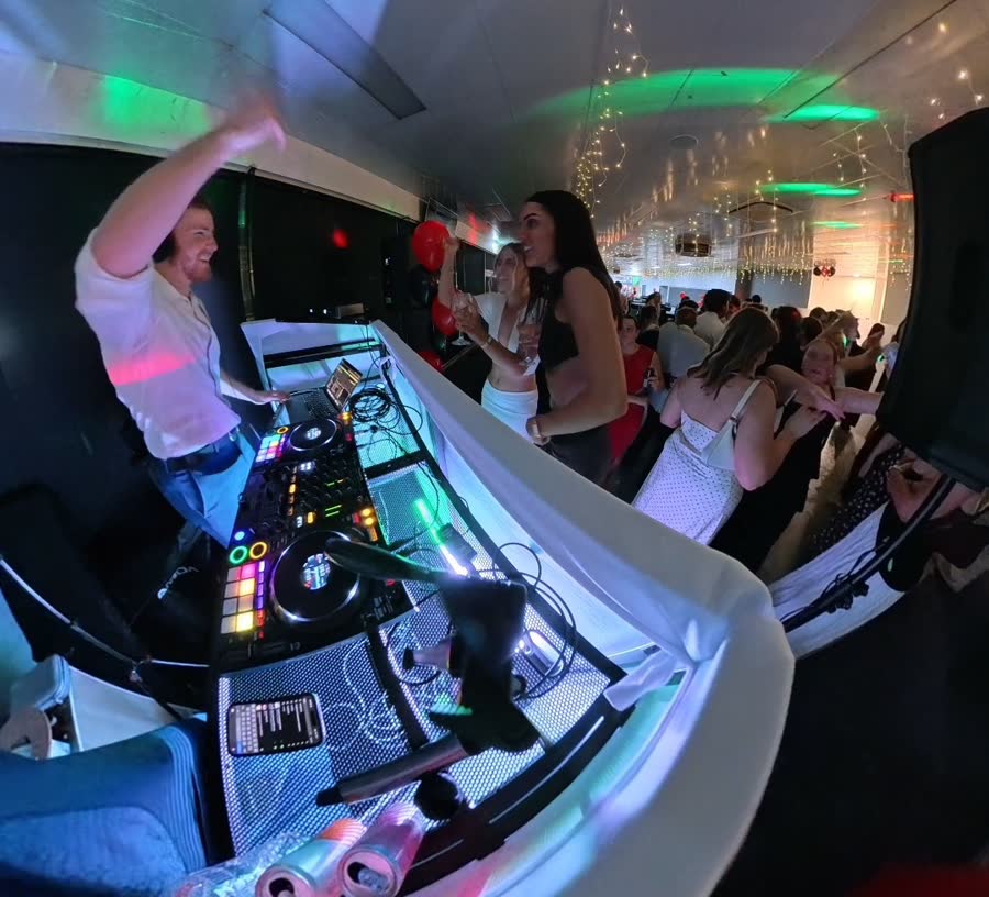 Tom waving behind the decks with guests dancing beside the DJ booth