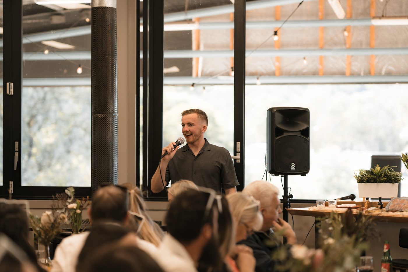 Tom hosting as MC and speaking to seated guests at a reception